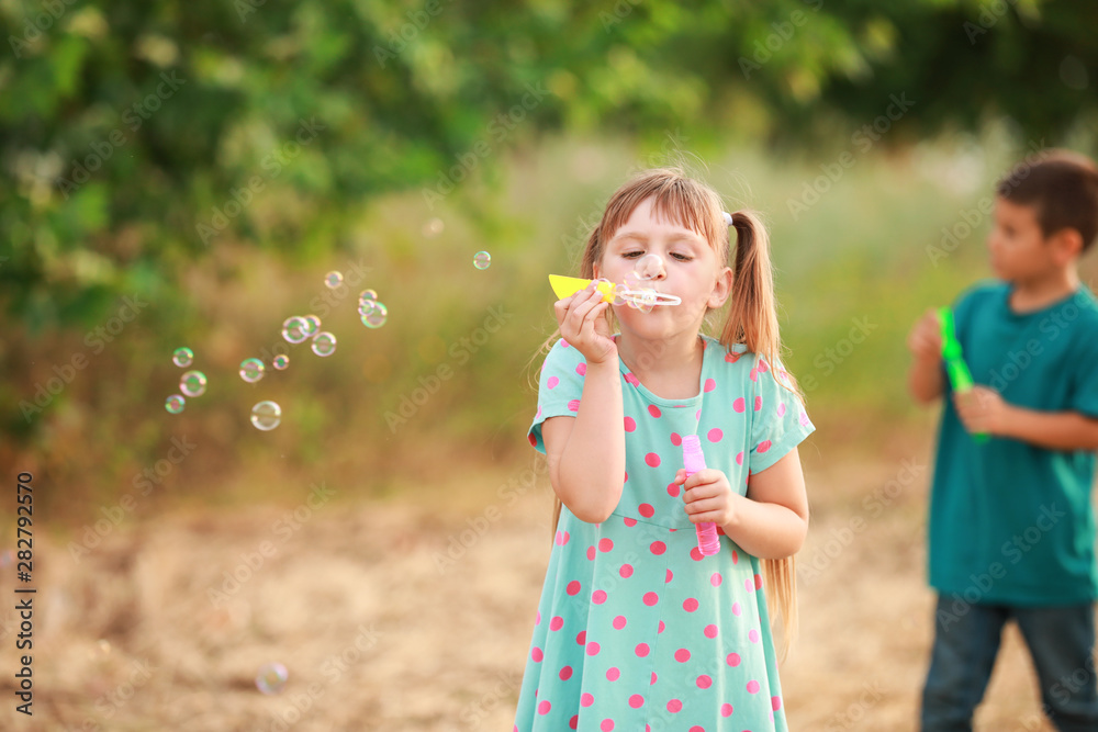 Cute little girl blowing soap bubbles outdoors
