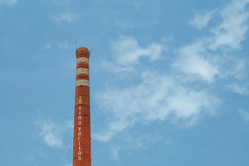 Smokestack in shape of wine bottle neck with text In vino veritas. Industrial chimney on cloud sky background with copy space. Manufacturing of alcohol drinks concept. Latin quotation of Roman Empire