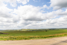 A Long Dirt Road In Rural North Dakota With A Bright Blue Sky With Clouds In The Horizon