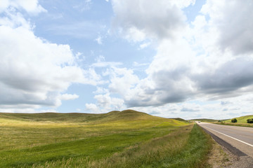 a long dirt road in rural North Dakota with a bright blue sky with clouds in the horizon