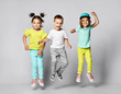© FAB.1 - Three excited kids in fashion outfits, jumping over the light background. Two sisters and brother, friends in fashionable clothes