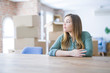 © Krakenimages.com - Young woman sitting on the table with cardboard boxes behind her moving to new home looking to side, relax profile pose with natural face with confident smile.