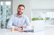 © Krakenimages.com - Handsome man working using computer laptop and drinking a cup of coffee with a happy face standing and smiling with a confident smile showing teeth