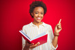 © Krakenimages.com - African american woman reading a book over red isolated background very happy pointing with hand and finger to the side