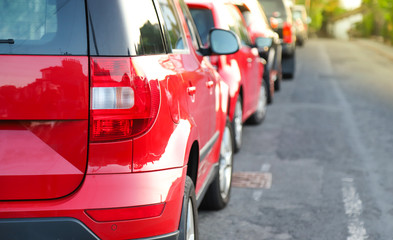 Closeup of rear, back side of red car with  other cars parking in outdoor parking area beside the street. 