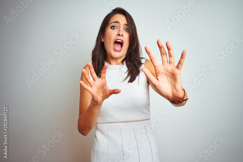 Cuadros en Lienzo Young beautiful woman wearing dress standing over white isolated background afraid and terrified with fear expression stop gesture with hands, shouting in shock