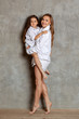 © nazarovsergey - Indoor portrait of a beautiful mother with her charming little daughter posing against a gray wall.