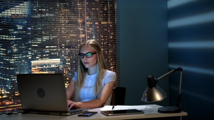 Beautiful female programmer working on the computer in modern office in the evening. The skyscrapers are in the background.