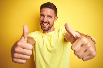 Young handsome man wearing casual yellow t-shirt over yellow isolated background approving doing positive gesture with hand, thumbs up smiling and happy for success. Winner gesture.