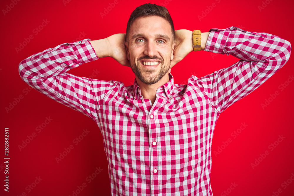 Young handsome man over red isolated background relaxing and stretching, arms and hands behind head and neck smiling happy