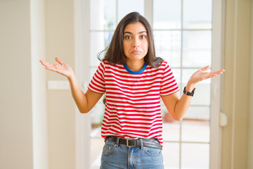 Young beautiful woman wearing casual t-shirt clueless and confused expression with arms and hands raised. Doubt concept.