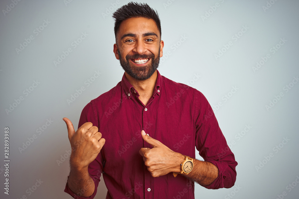 Young indian man wearing red elegant shirt standing over isolated grey background Pointing to the back behind with hand and thumbs up, smiling confident - obrazy, fototapety, plakaty 