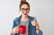 Young beautiful redhead woman drinking cup of coffee over isolated white background happy with big smile doing ok sign, thumb up with fingers, excellent sign