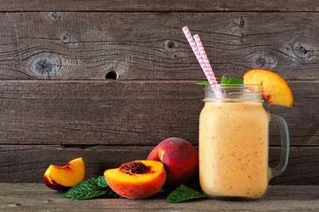 Wall Mural - peach smoothie in a mason jar glass with scattered fruit. side view with a rustic dark wood backgrou