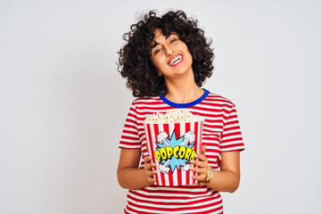 Wall Mural - Young arab woman with curly hair holding pack of popcorns over isolated white background with a happy face standing and smiling with a confident smile showing teeth