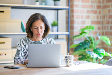 Sticker - Middle age senior woman sitting at the table at home working using computer laptop with a confident expression on smart face thinking serious