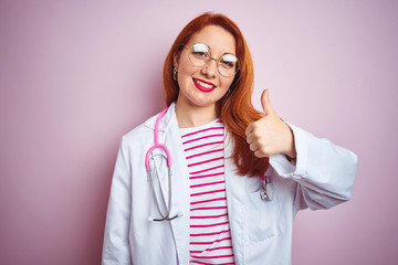 Sticker - Young redhead doctor woman wearing glasses over pink isolated background doing happy thumbs up gesture with hand. Approving expression looking at the camera with showing success.