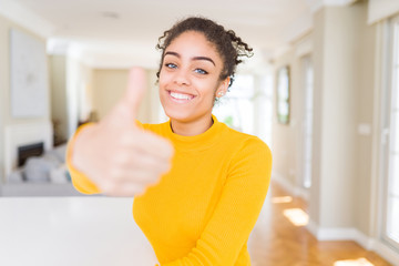 Beautiful young african american woman with afro hair doing happy thumbs up gesture with hand. Approving expression looking at the camera showing success.