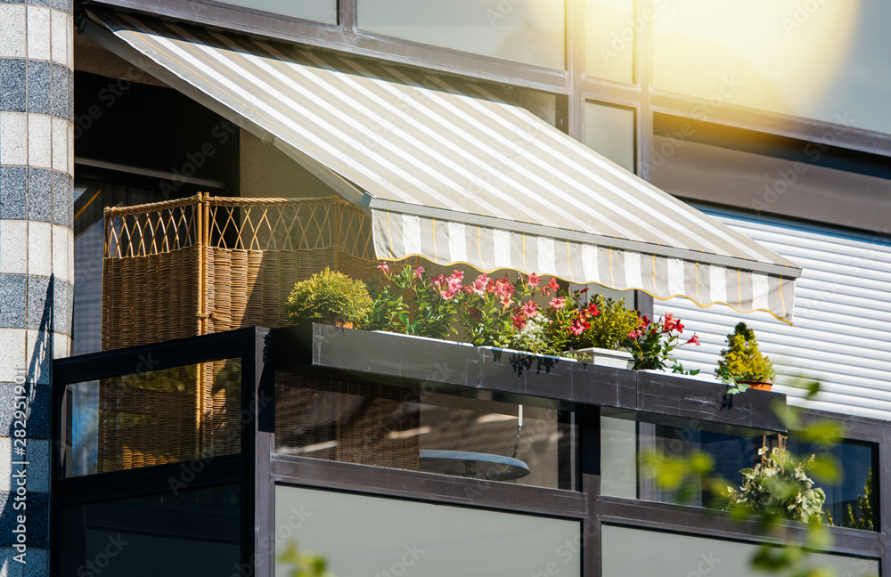 French balcony with beautiful awning and flowers covered with rays of sun - protection during hot weather and radiation - obrazy, fototapety, plakaty 