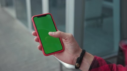 Close up hands man holding a smartphone touching phone with vertical green screen red case on background walk near airport street message business male device digital equipment internet slow motion