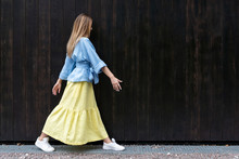 Young European Girl, Natural Long Hair, Beautiful Face. Long Yellow Skirt, Blue Wide Jacket, White Sneakers Cool To Pose Black Boards Background. Comfortable Linen Womens Clothing.