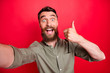 Photo of handsome overjoyed ecstatic man wearing grey shirt self shooting when thumbing up to you while isolated with red background