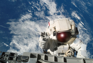 Wall Mural - the astronaut in a space suit, waves a hand, at the space station, in an outer space. elements of th