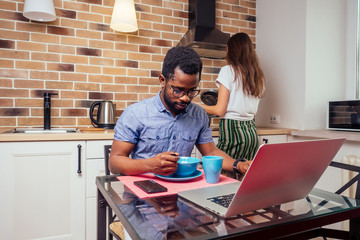 african male useing laptop at home , european woman pouring soup into a plate from stewpan brick wall ,cooker hood background