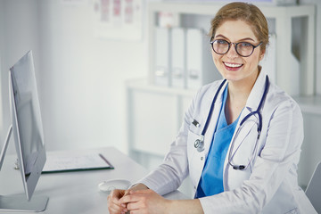 Wall Mural - Beautiful young smiling female doctor sitting at the desk