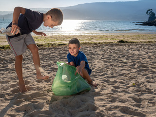 two young boys collecting rubbish and plastic on the beach