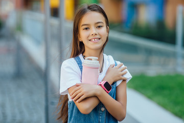 Portrait of small girl,  hands holding pink thermos, on hands smart watches. Running.