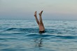 A man is doing a handstand in the sea and only his feet can be seen. Other people are swimming nearby