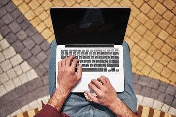 Wall Mural - Blogging. Top view of man working on laptop while sitting outdoors