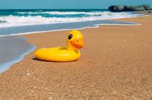 Inflatable Rubber Duck Swimming Ring On The Sand Near Sea On The Beach
