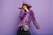 Laughing curly woman in sparkle sunglasses dancing on purple background. Happy girl in fluffy coat enjoying photoshoot in winter clothes.