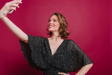 Fashionable white woman with beautiful smile making selfie in confident pose. Indoor portrait of winsome girl in trendy black attire taking picture of herself.