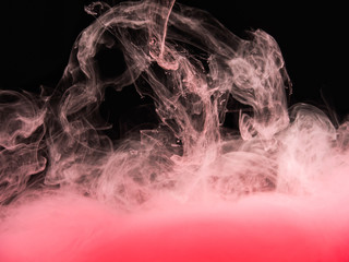 Drop of pink paint dissolving into liquid, isolated on black background, close up view. Pink acrylic cloud under water. Abstract black background for overlays design, screen blending mode layer