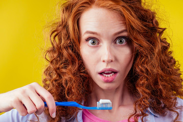 redhaired ginger woman brushing teeth with toothpaste eco paste on yellow studio background