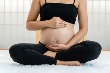 Closeup Asian Pregnant sitting and holds hands on belly in japanese style house on the white carpet, pregnant concept, preparing to be motherhood with good healthy