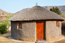Traditional African Round Clay House With Thatched Roof In Village, Kingdom Of Lesotho, Southern Africa, Ethnic Basotho People National Old Home Close Up, Drakensberg Mountains Landscape Background