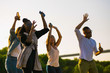 Smiling young people dancing with raised hands. Group of friends relaxing in park during sunset. Leisure concept