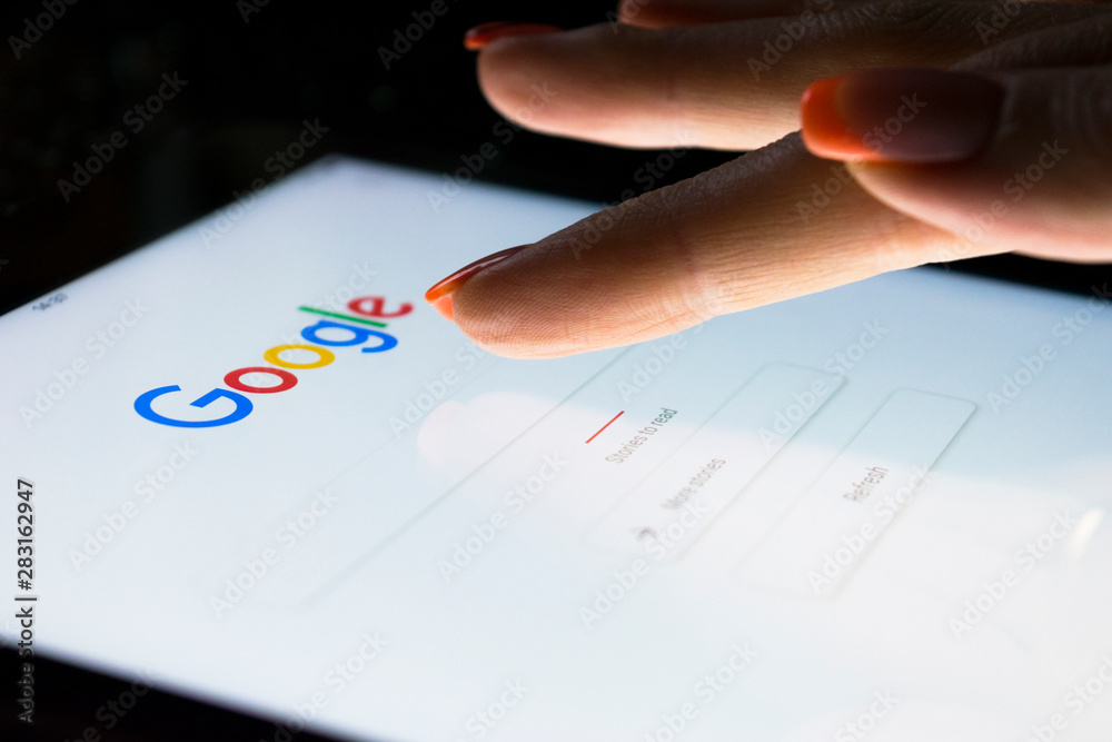Sankt-Petersburg, Russia, November 8, 2017:  A woman's hand is touching screen on tablet computer iPad pro at night for searching on Google search engine. Google is popular Internet search engine