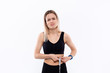 © ianachyrva - Young blond woman in a black sportswear with smart watches is upset checking waist after workout with the tape measure standing over white background.