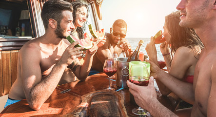 Group of young people having fun drinking and eating watermelon - Happy friends making boat party in summer vacation - Travel and friendship concpet - Focus on left guy face