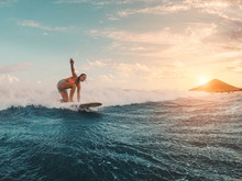 Fit Female Athlete Surfing At Sunset - Surfer Woman Performing Outdoor Inside Ocean - Extreme Sport, Travel, Healthy Lifestyle, Adventure And Vacation Concept - Focus On Her Body