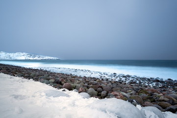 Wall Mural - long exposure of the surf breaking over stone boulders on a snow covered beach