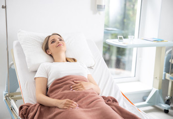 Beautiful young woman lying in bed at modern clinic