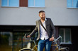 © oes - Portrait of handsome young red bearded man in casual clothes using phone, drink coffee and looking away and smiling while leaning on his bike, standing outdoors. Office and business center background