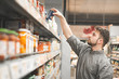 Man with a beard is in the department of canned vegetable supermarket and takes a can from the shelf. The buyer selects canned food in the grocery store.