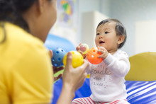 Young Little Asian Baby Holding Balls And Toys Playing With Female Preschool Teacher In Classroom. Kid Looking At Nanny That Teaching Her With Smile, Enjoy Learning In Education Development Class.